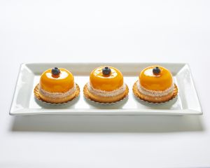 Three yellow glazed pastries topped with a single blueberry each are arranged in a row on a rectangular white plate.