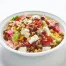 A white bowl filled with chopped salad featuring garbanzo beans, roasted corn, feta cheese, red onions, tomatoes, savory granola, dried cranberries, and mustard-dill vinaigrette on a white background.