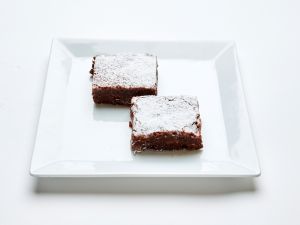 Two Brownies topped with powdered sugar on a square white plate.