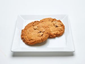 Two Chocolate Chip Cookies from Chocolate Chip Cookie on a square white plate against a plain background.