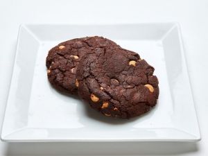 Two dark chocolate cookies with peanut butter chips on a white square plate.