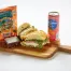 The Prosciutto & Burrata Cheese Sandwich Box includes a halved sandwich, a brownie, Hawaiian BBQ chips, and a can of San Pellegrino sparkling drink.