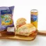 The Turkey & Avocado Sandwich Box includes a halved sandwich, brownie, Maui onion chips, and a San Pellegrino lemon soda, all served on a wooden board against a white background.
