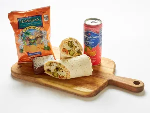 The Roasted Vegetables Sandwich Box includes a halved wrap, brownie, Hawaiian Luau BBQ chips, and a Sanpellegrino soda, all served on a wooden board.