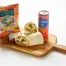 The Roasted Vegetables Sandwich Box includes a halved wrap, brownie, Hawaiian Luau BBQ chips, and a Sanpellegrino soda, all served on a wooden board.