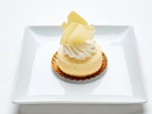 A cheesecake sits on a gold-bedecked white square plate, adorned with white chocolate shards and cream.