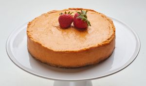 Cheesecake on a white cake stand topped with two strawberries.