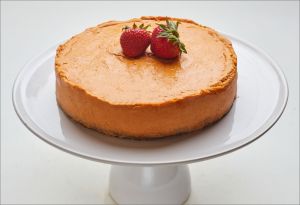 Orange cheesecake on a white cake stand, topped with two strawberries.