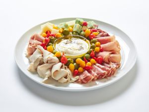 A white plate with assorted cured meats, cheeses, and colorful peppers arranged around a bowl of creamy dip in the center—perfect for sharing at parties or adding to your favorite platters.