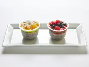 Chia Seed Pudding served in two cups on a white plate—one topped with mango and coconut, the other with house-made granola and berry compote.