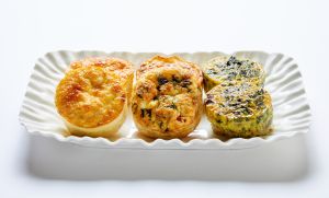 A white rectangular platter holds four mini frittatas with different fillings, arranged in a row on a white background.